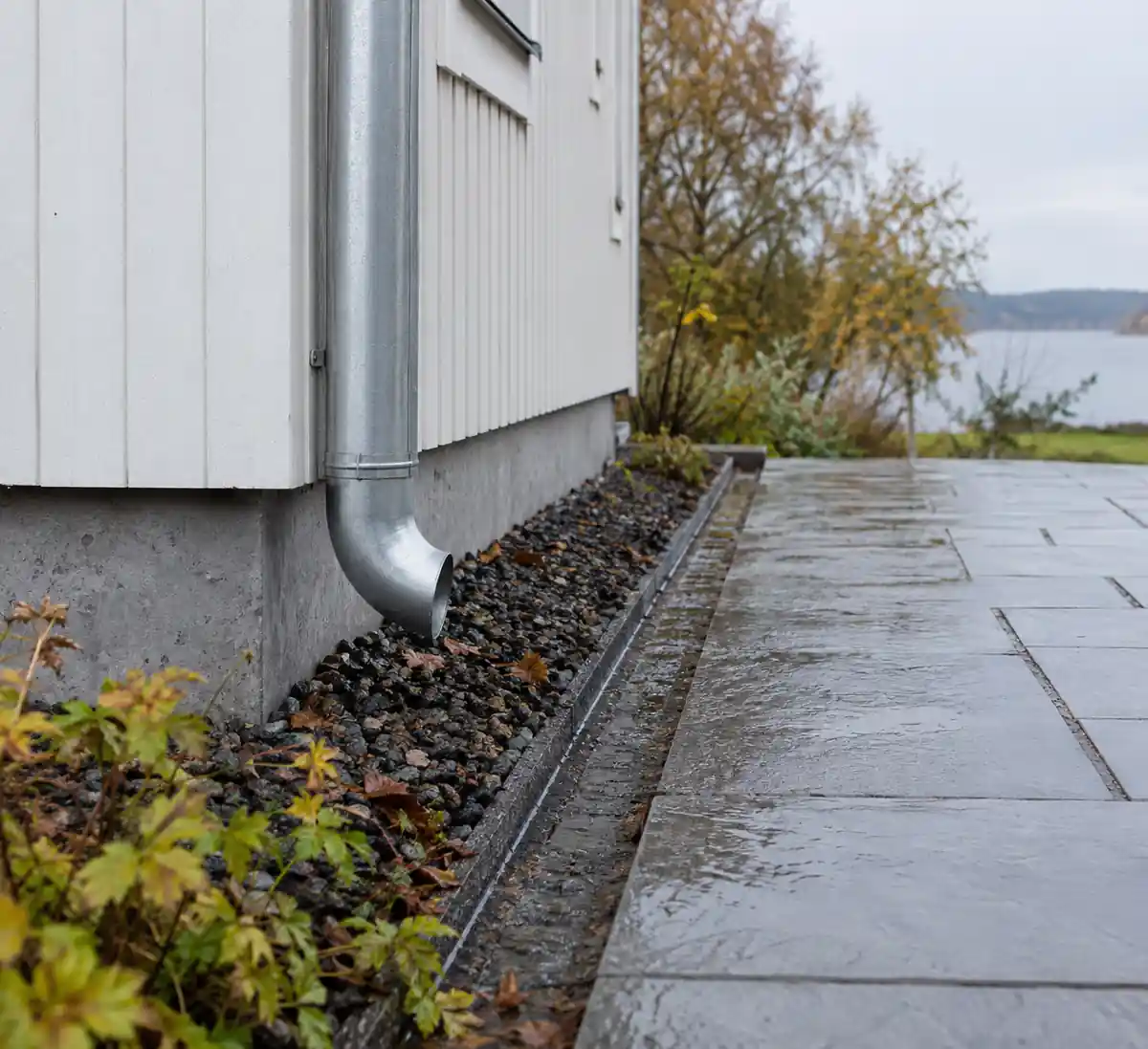 Stuprör som mynnar i en stenkista intill husgrunden, med en ränna som leder regnvattnet bort från huset